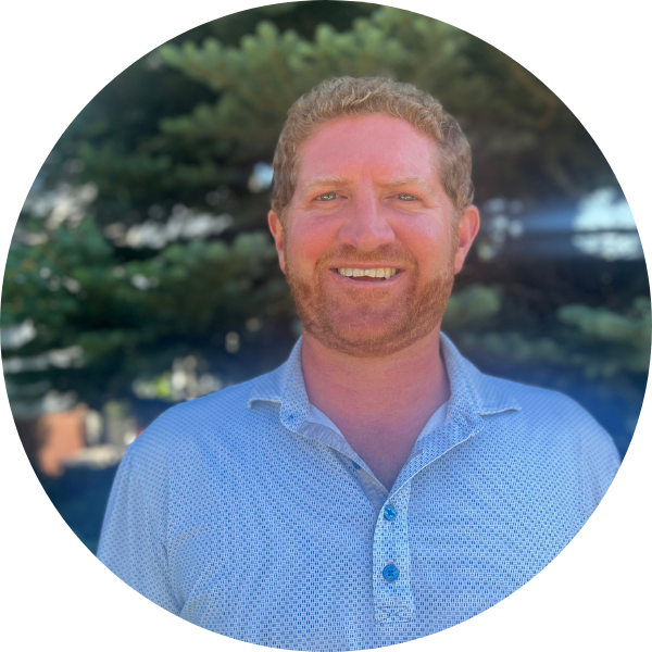 Headshot of Matt Kireker with blue shirt and tree in background.