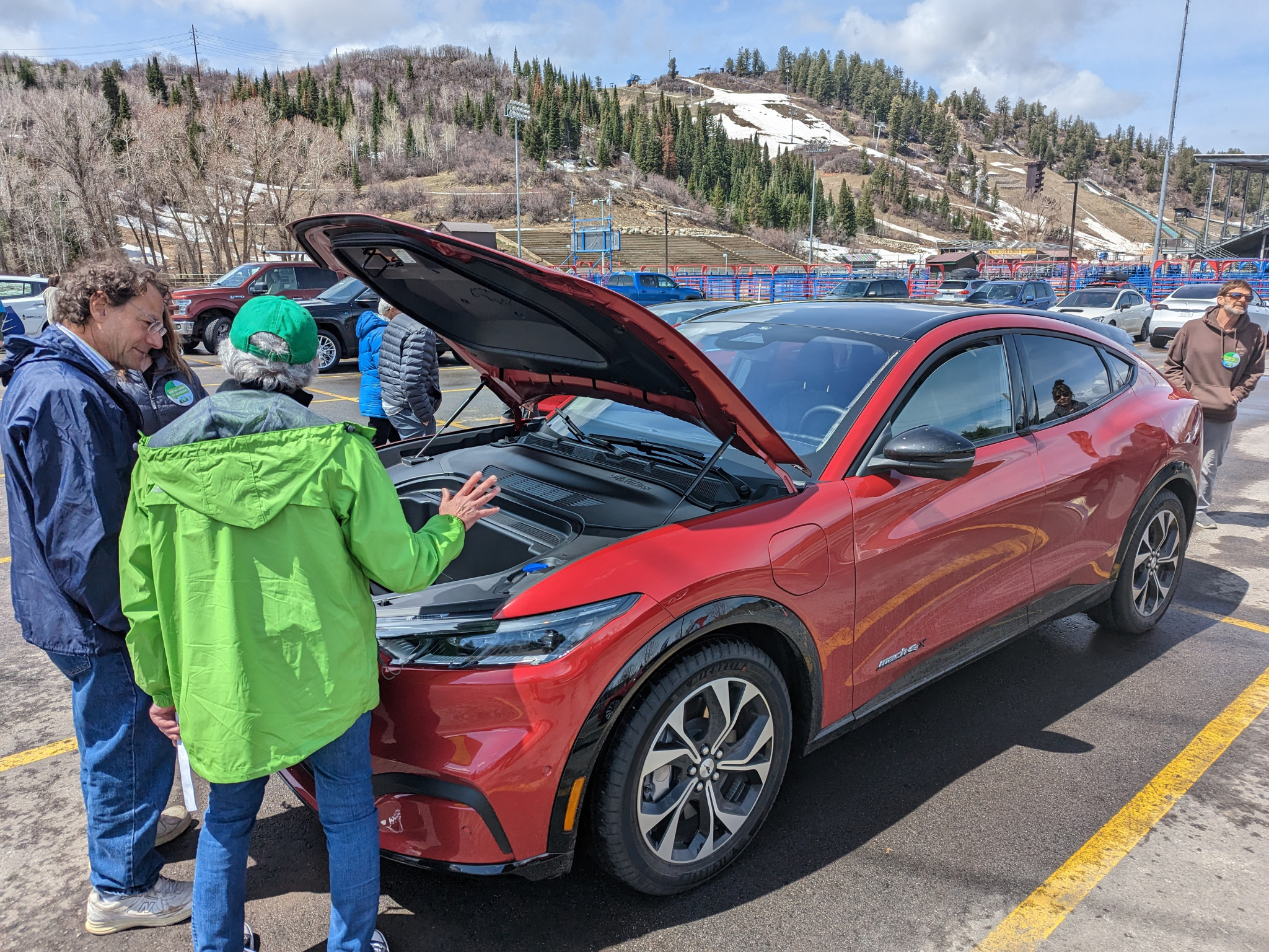 Two people standing together looking under the hood of a red electric vehicle in a parking lot.