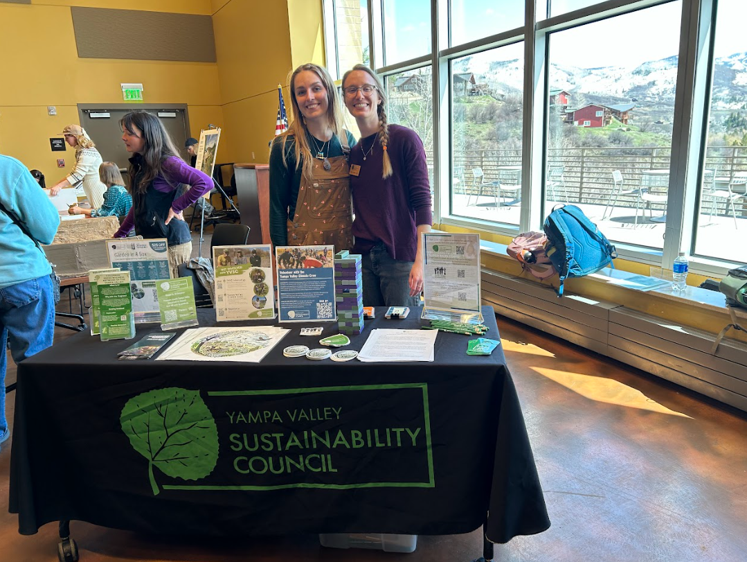Two people smile at an event in front of a table that reads "Yampa Valley Sustainability Council"