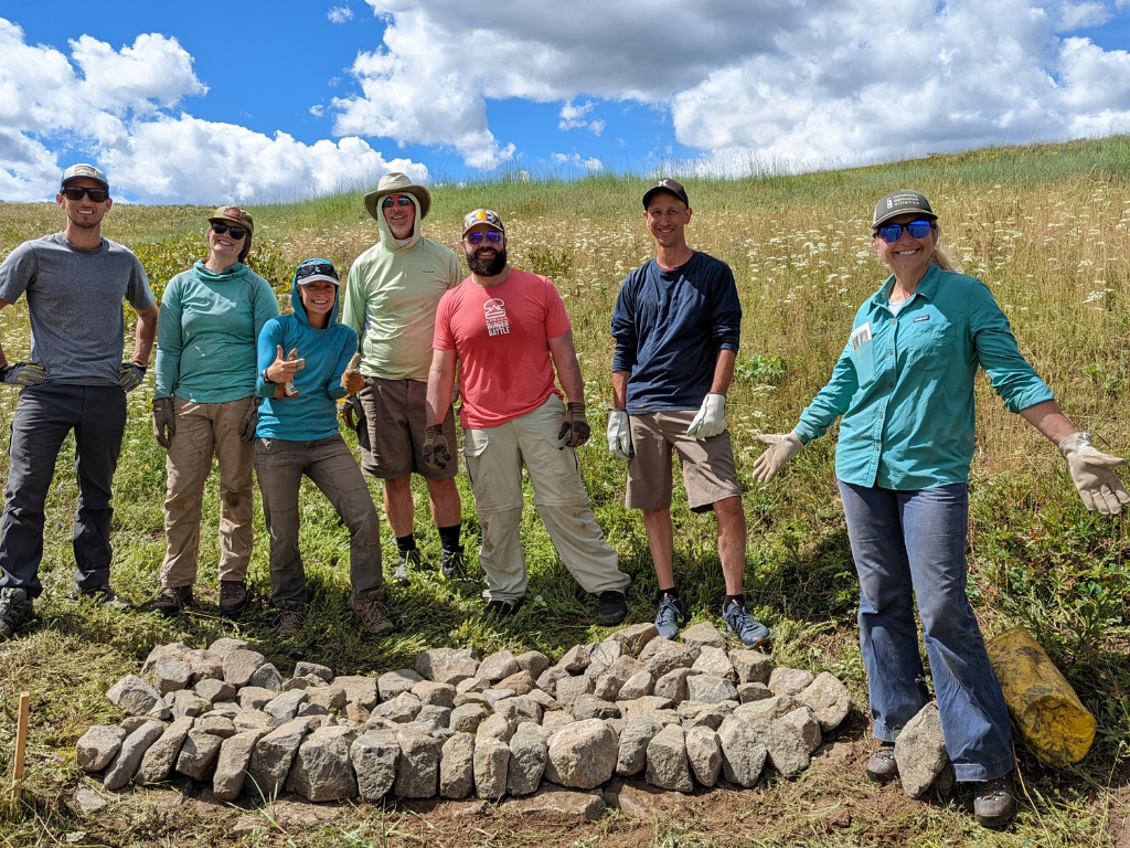 Photo of a group posing in front of a rock structure in a wet meadow.